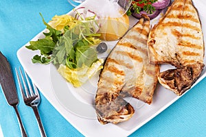 Steak of river fish with white meat, served with vegetables, lemon and arugula and tomato salad