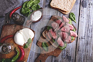 Steak sandwich, sliced roast beef, cheese,spinach leaves,tomato. Rustic,on a wooden surface