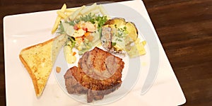 Steak set of pork serve with baked potato, butter, vegetable salad, french fried and bread butter toast served in ceramic plate