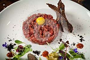 Steak tartare. Horseradish creme, black bread, baguette chips on white plate. Delicious healthy raw meat food closeup