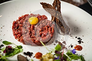 Steak tartare. Horseradish creme, black bread, baguette chips on white plate. Delicious healthy raw meat food closeup