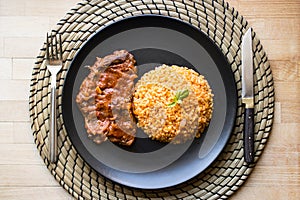 Steak with tomato sauce and bulgur rice in a black plate.