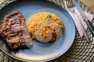 Steak with tomato sauce and bulgur rice in a black plate.