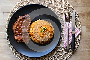 Steak with tomato sauce and bulgur rice in a black plate.