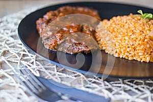 Steak with tomato sauce and bulgur rice in a black plate.