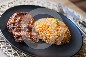 Steak with tomato sauce and bulgur rice in a black plate.