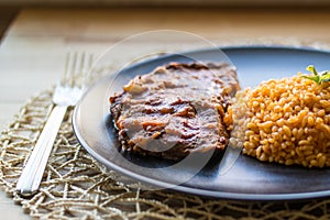 Steak with tomato sauce and bulgur rice in a black plate.