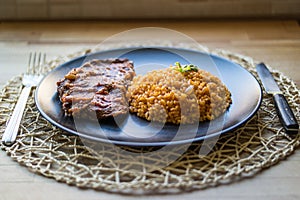 Steak with tomato sauce and bulgur rice in a black plate.