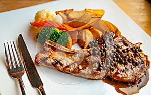 Steak topped with sauce and pepper serve with potato fried and carrots, cauliflower and broccoli steamed. Steak on white plate