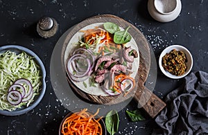 Steak tortilla with pickled carrots and cabbage on a wooden cutting board on dark background