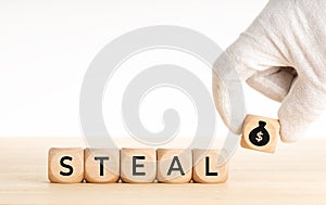 Steal concept. Hand picking a wooden block whit money bag icon and text on wooden dice. Copy space