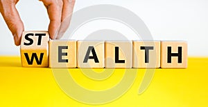 Stealth wealth symbol. Businessman turns the wooden cube and changes the word `wealth` to `stealth`. Beautiful yellow table, w