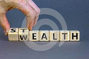 Stealth wealth symbol. Businessman turns wooden cubes and changes the word `wealth` to `stealth`. Beautiful grey background.