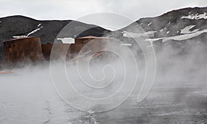 Steam from active volcano in front of abandoned Storage Tanks from a whaling station at Whaler`s Bay, Deception Island