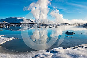 Steam from a geothermal plant set against a bright blue sky and reflected in a lake beside the Blue Lagoon