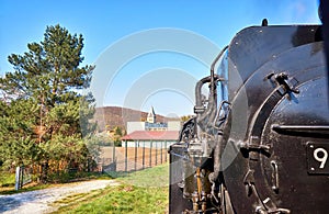Steam locomotive drives past a sports field with a church tower in the background. Dynamic due to motion blur