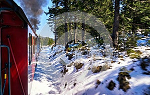 Steam locomotive drives through the trees with a blue sky. Winter in the snow covered mountains. Dynamics through motion blur