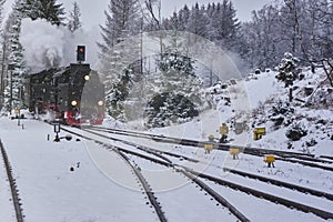 Steam locomotive with smoking and steaming chimney is heading for the snowy switches of the tracks in the forest in winter time