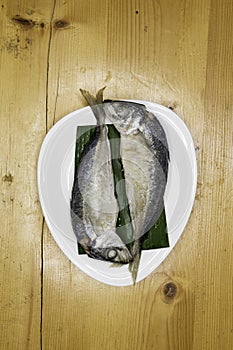 Steam with mackerel in white dish on wood table