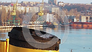 Steam rises from ship funnel as tugboat navigates river. Industrial port cranes, vessels, logistics. Early morning light