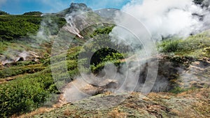 Steam and smoke rise from the fumarole on the hillside.