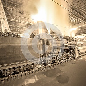 Steam train arrives to the station at night time.