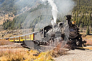 Steam train with yellow wagons going uphill