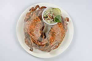 Steamed blue crab on white plate with spicy seafood sauce.