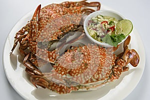 Steamed blue crab on white plate with spicy seafood sauce.