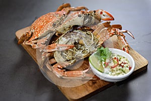 Steamed blue crab on wooden plate with spicy seafood sauce.