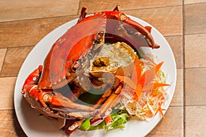 Steamed crab or Boiled crab fresh with crab`s spawn in white dish showing the delicious crab`s eggs inside its shell on wood table