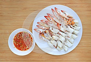 Steamed crab meat in white circle plate with spicy chili seafood dipping sauce on wooden board background. Ready to eat. Top view