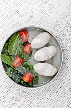 Steamed cutlets of three kinds of white meat with fresh spinach and tomatoes. Top view