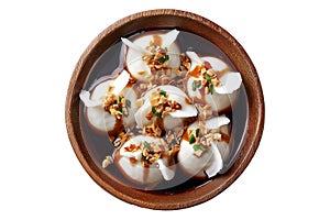 Steamed Faikakai dumplings topped with soy-based glaze, coconut syrup and sesame seeds in wooden bowl on white background