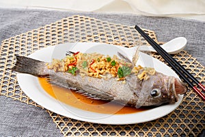STEAMED GAROUPA IN TRADITIONAL SAUCE with chopsticks served in dish isolated on table top view of singapore food photo