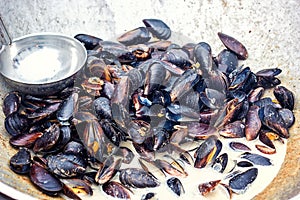 Steamed mussels in white wine sauce cooking at large metallic pan. Fresh mussels at grill pan. Seafood barbecue outdoors. Picnic h