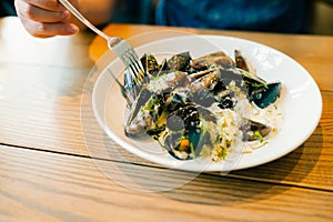 Steamed mussles in white bowl on table with hands