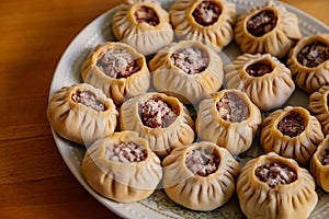 Steamed national Mongolian food dumpling Buuz filled with minced beef, white plate, wooden table, Close up east Siberian Buryats