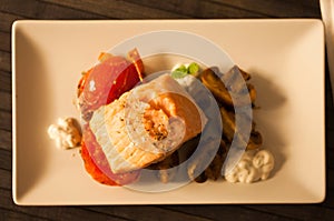 Steamed salmon fillet on a pillow of fried mushrooms and tomatoes on a white plate. top view
