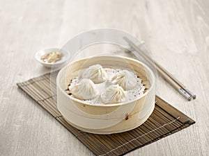 Steamed Xiao Long Bao with chopsticks served in a dish isolated on mat side view on grey background