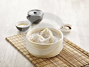 Steamed Xiao Long Bao served in a wooden bowl isolated on mat side view on grey background