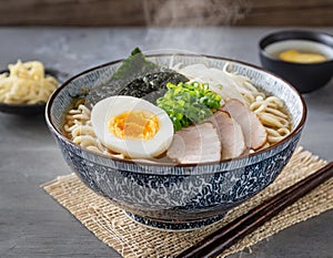 A steaming bowl of ramen noodles topped with slices of tender pork belly, soft-boiled egg