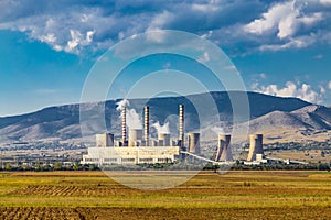 Steaming coal power plant over yellow agriculture field on the mountains background. Ð•nvironmental pollution concept