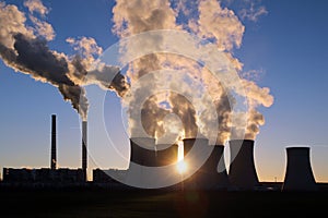 Steaming cooling towers of coal power plant against the sun photo