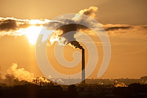 Steaming cooling towers and smoking industrial stacks against sunset gradient sky
