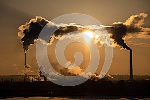 Steaming cooling towers and smoking industrial stacks against sunset gradient sky