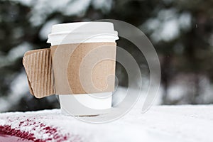 Steaming Cup of Hot Coffee or Tea standing on the Outdoor Table in Snowy Winter Morning. Cozy Festive paper cupwith a Warm Drink i