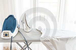 Steaming iron on ironing board near window with copy space