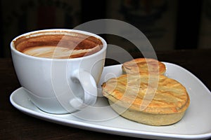 Steaming latte and meat pies on white plate