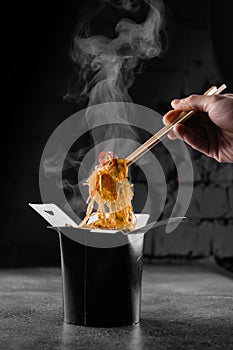 Steaming rice noodles in wok box on black background. Fast food delivery service. Takeaway chinese street meal. Udon in